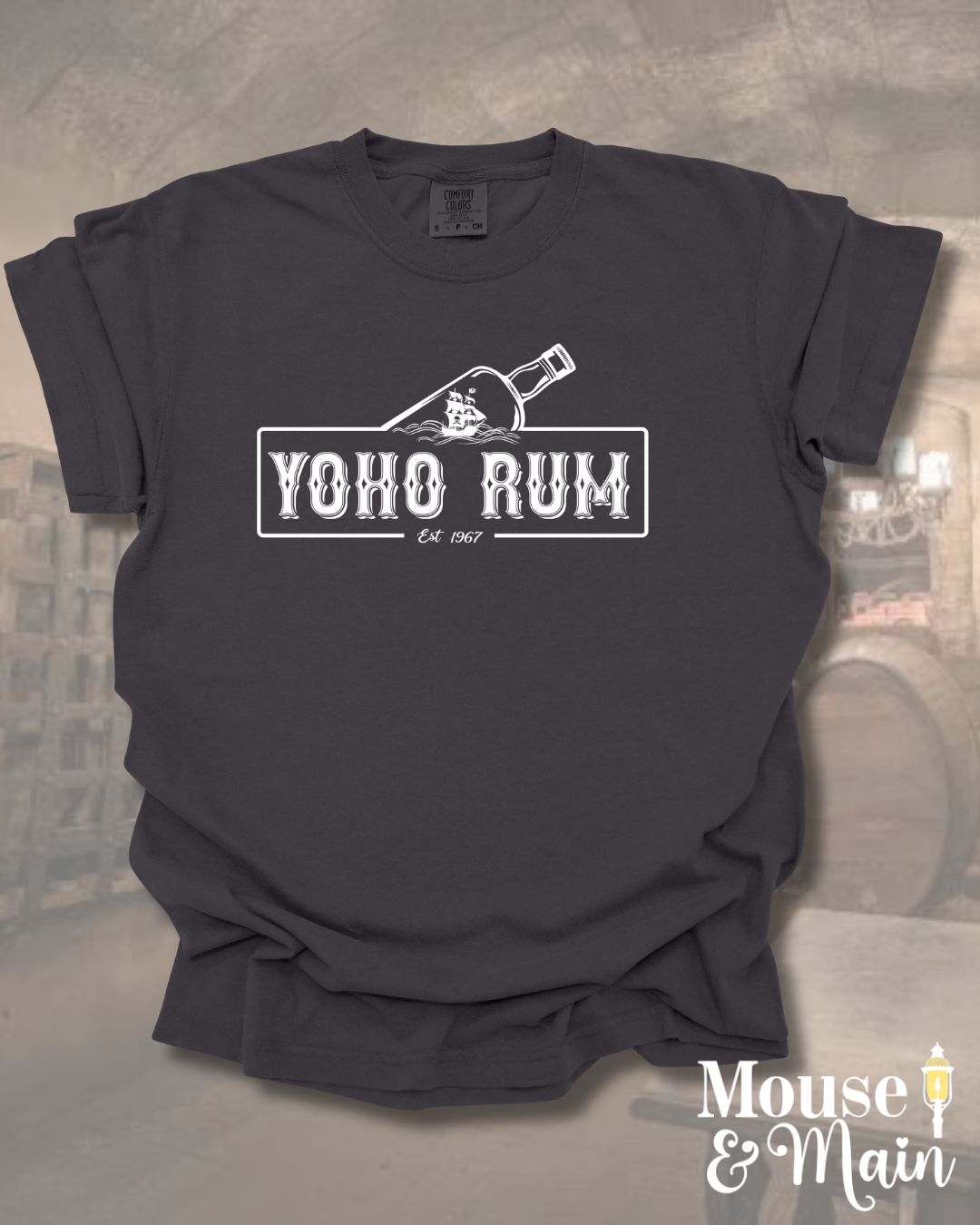Flat lay of pirate-themed t-shirt reading 'YOHO RUM – Est. 1967' with vintage bottle design, styled for theme park or cruise wear.