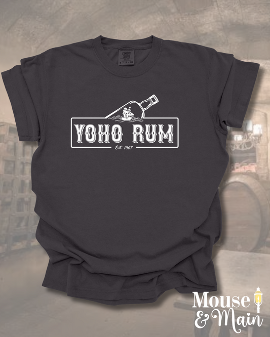 Flat lay of pirate-themed t-shirt reading 'YOHO RUM – Est. 1967' with vintage bottle design, styled for theme park or cruise wear.